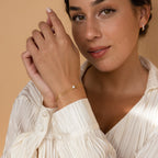 Woman wearing a cream blouse, gold earrings, and the Duo Chain Diamond Bracelet with a single gemstone, smiling softly—the ideal minimalist bracelet for an anniversary gift.