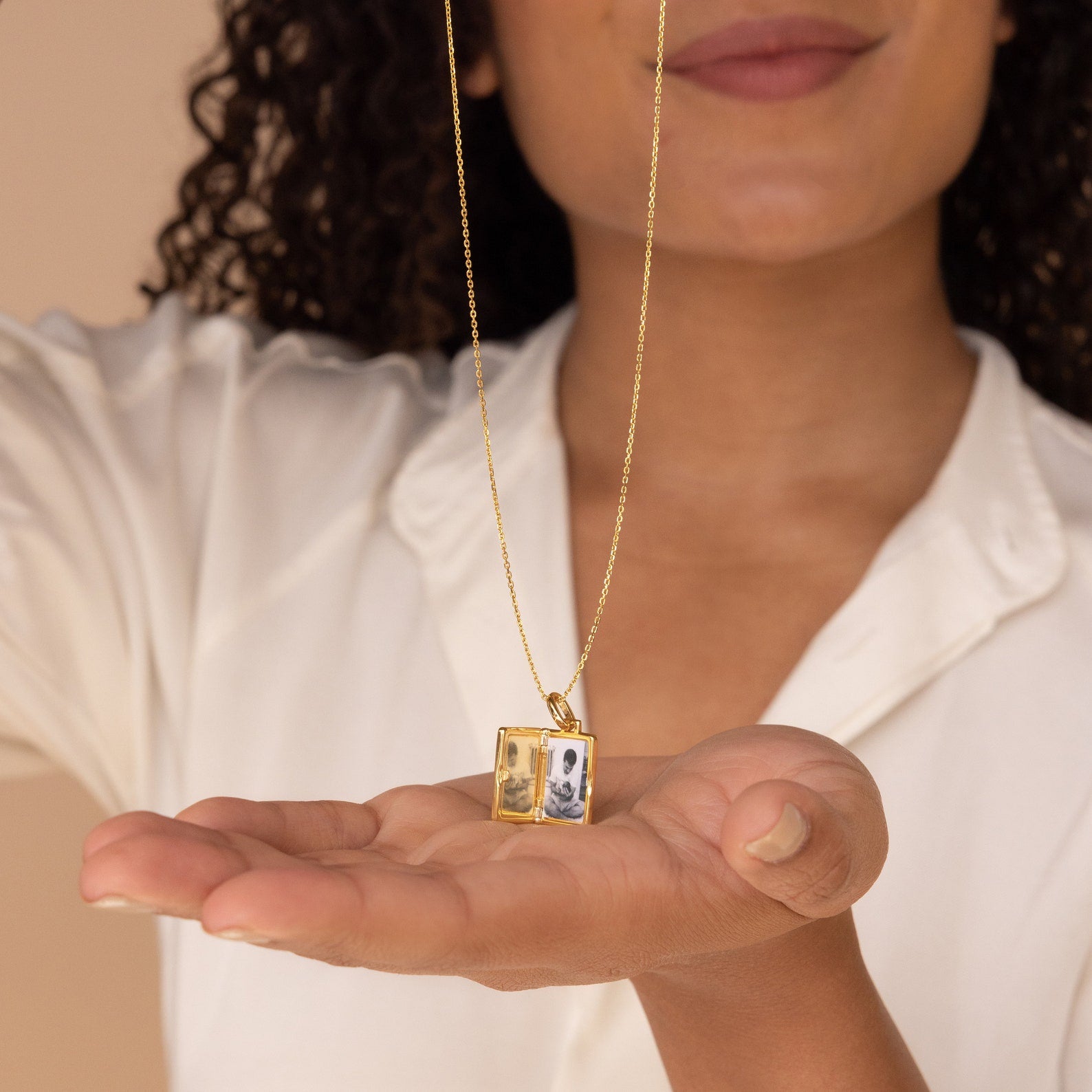 A woman holds the Onyx Locket Necklace, a gold charm showcasing two tiny black and white photos—making it a unique, personalized gift.