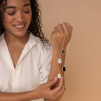 A smiling woman in a cream blouse holds three gold and silver pendant necklaces, featuring the Onyx Locket Necklace, against a beige background.