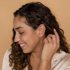 A woman with curly hair smiles, her look glowing with Opal Drop Studs that add a touch of iridescent elegance.