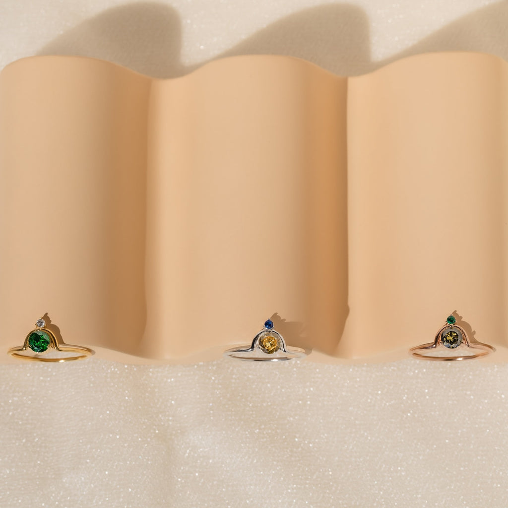 The Duo Vintage Birthstone Ring with colored center stones rests on wavy beige fabric—an elegant personalized mom ring, ideal for Mother’s Day or as a thoughtful gift for new moms.