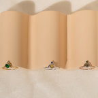 The Duo Vintage Birthstone Ring with colored center stones rests on wavy beige fabric—an elegant personalized mom ring, ideal for Mother’s Day or as a thoughtful gift for new moms.