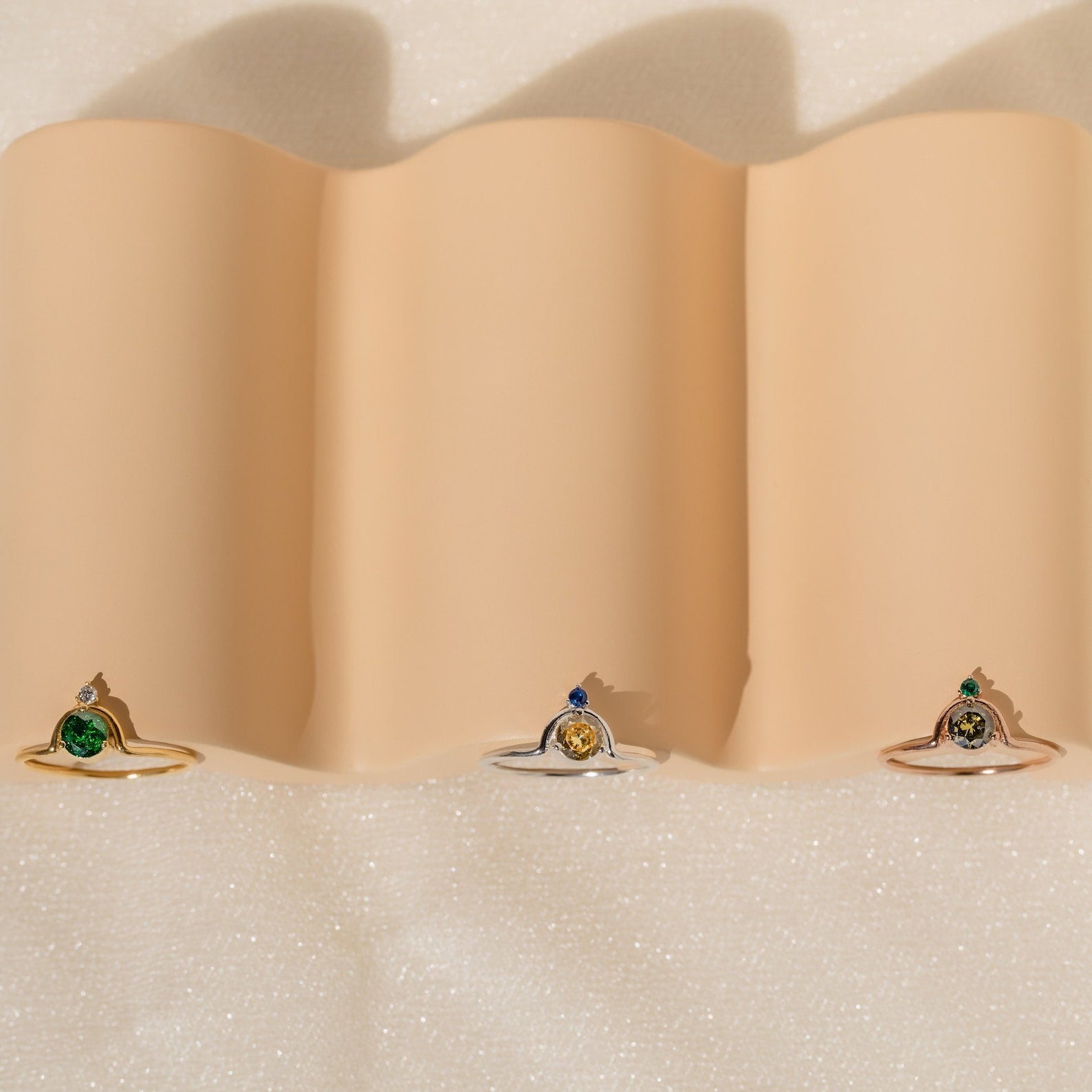 The Duo Vintage Birthstone Ring with colored center stones rests on wavy beige fabric—an elegant personalized mom ring, ideal for Mother’s Day or as a thoughtful gift for new moms.