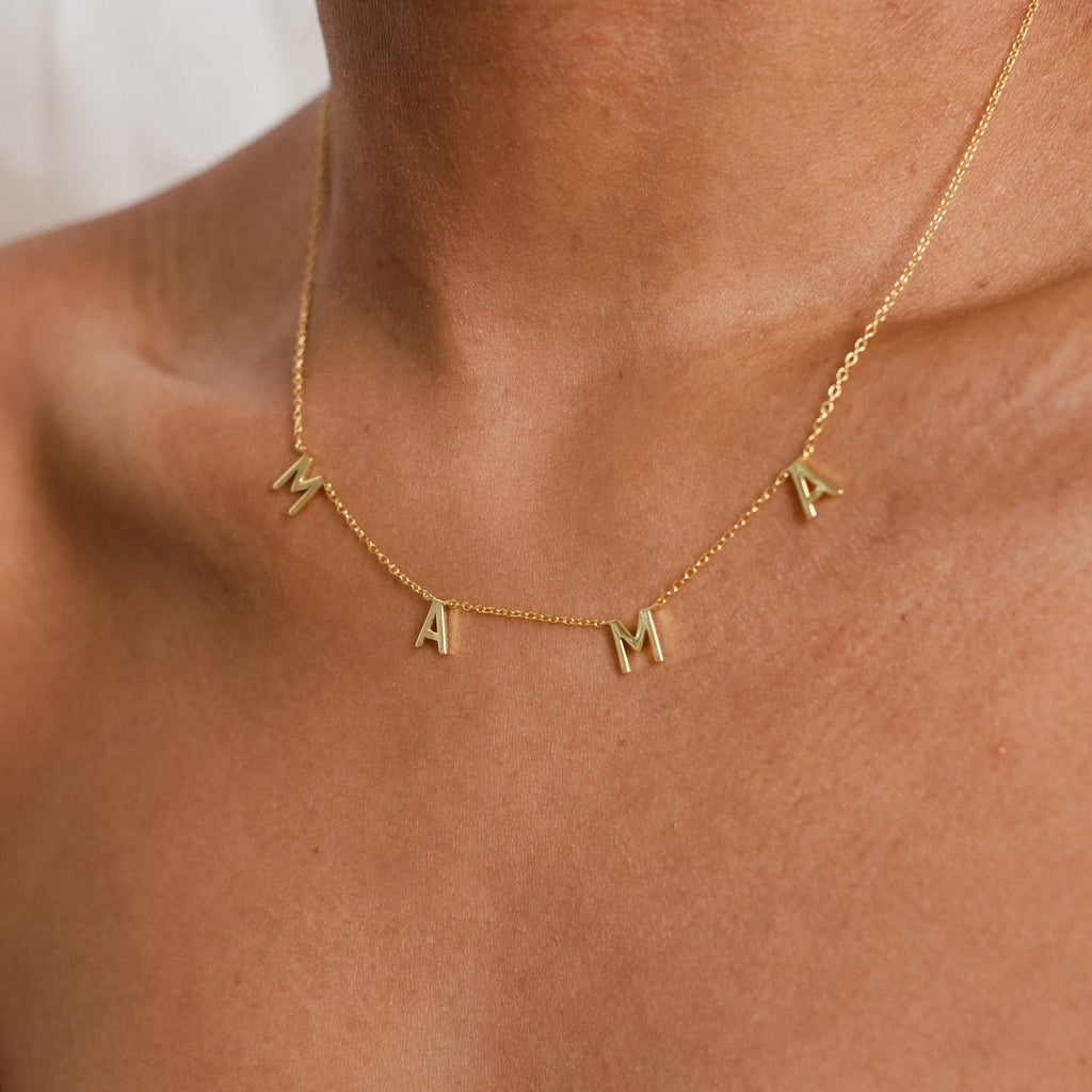 Close-up of a Mama Necklaces piece on a persons neck, showcasing letter charms that spell MAMA—an ideal gift for mom, beautifully crafted from elegant 925 sterling silver.