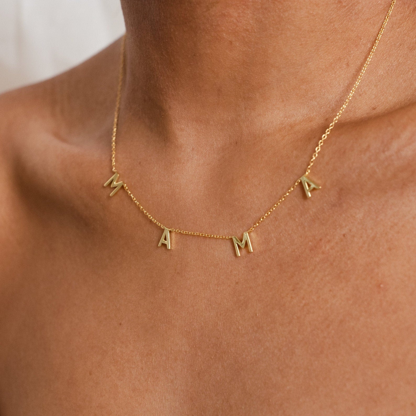 Close-up of a Mama Necklaces piece on a persons neck, showcasing letter charms that spell MAMA—an ideal gift for mom, beautifully crafted from elegant 925 sterling silver.