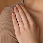 A hand with nude nails wears the Duo Vertical Baguette Ring—a delicate gold ring with two small red stones on the ring finger, making it a perfect personalized gift.