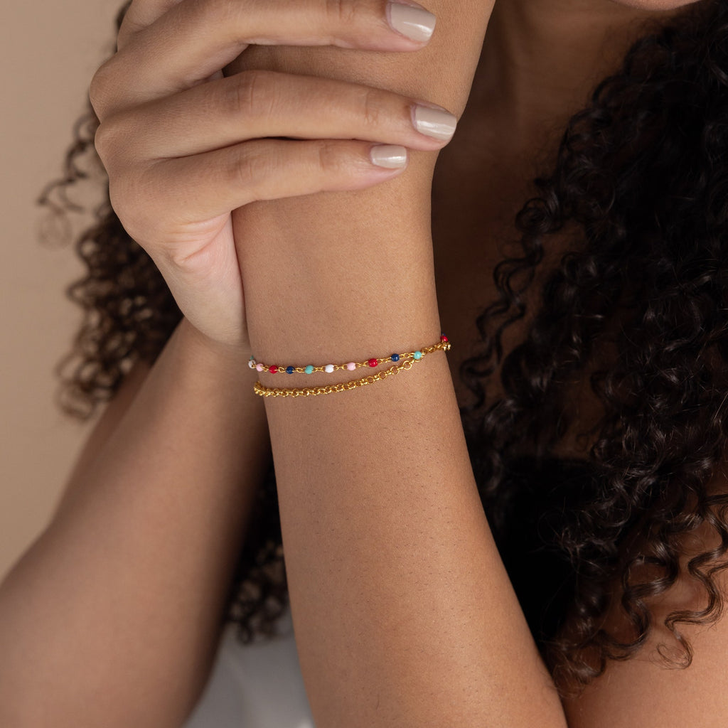 A woman with curly hair wears two delicate, colorful Rainbow Station Bracelets on her wrist.