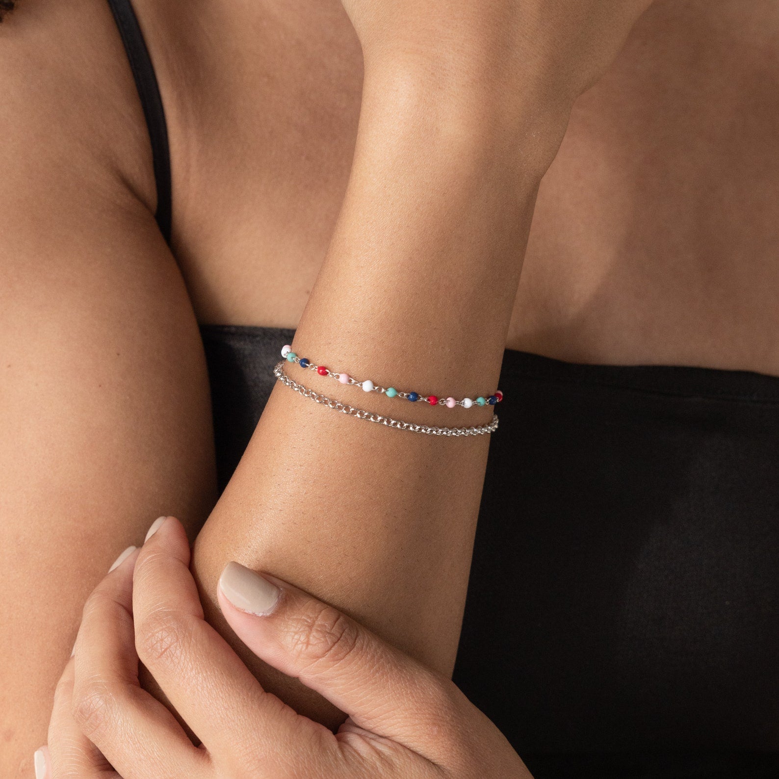 A woman wearing a black top and the Rainbow Station Bracelet, paired with other colorful beaded bracelets, her hands gently crossed.