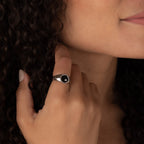 A woman with curly hair wearing the Natasha Black Signet Ring gently touches her hair and smiles slightly.