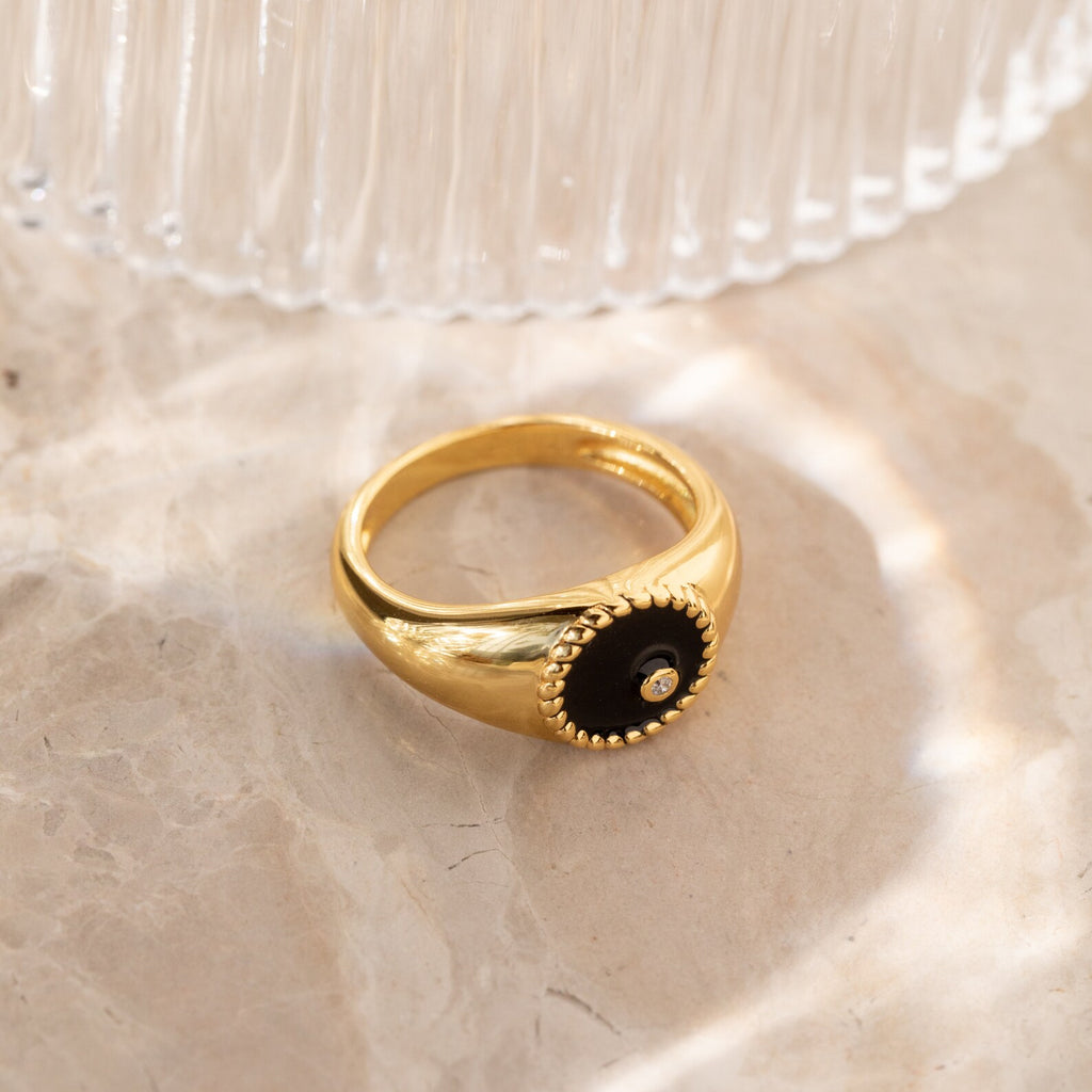 The Natasha Black Signet Ring features a black circular center with a small CZ diamond, elegantly displayed on marble.