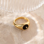The Natasha Black Signet Ring features a black circular center with a small CZ diamond, elegantly displayed on marble.