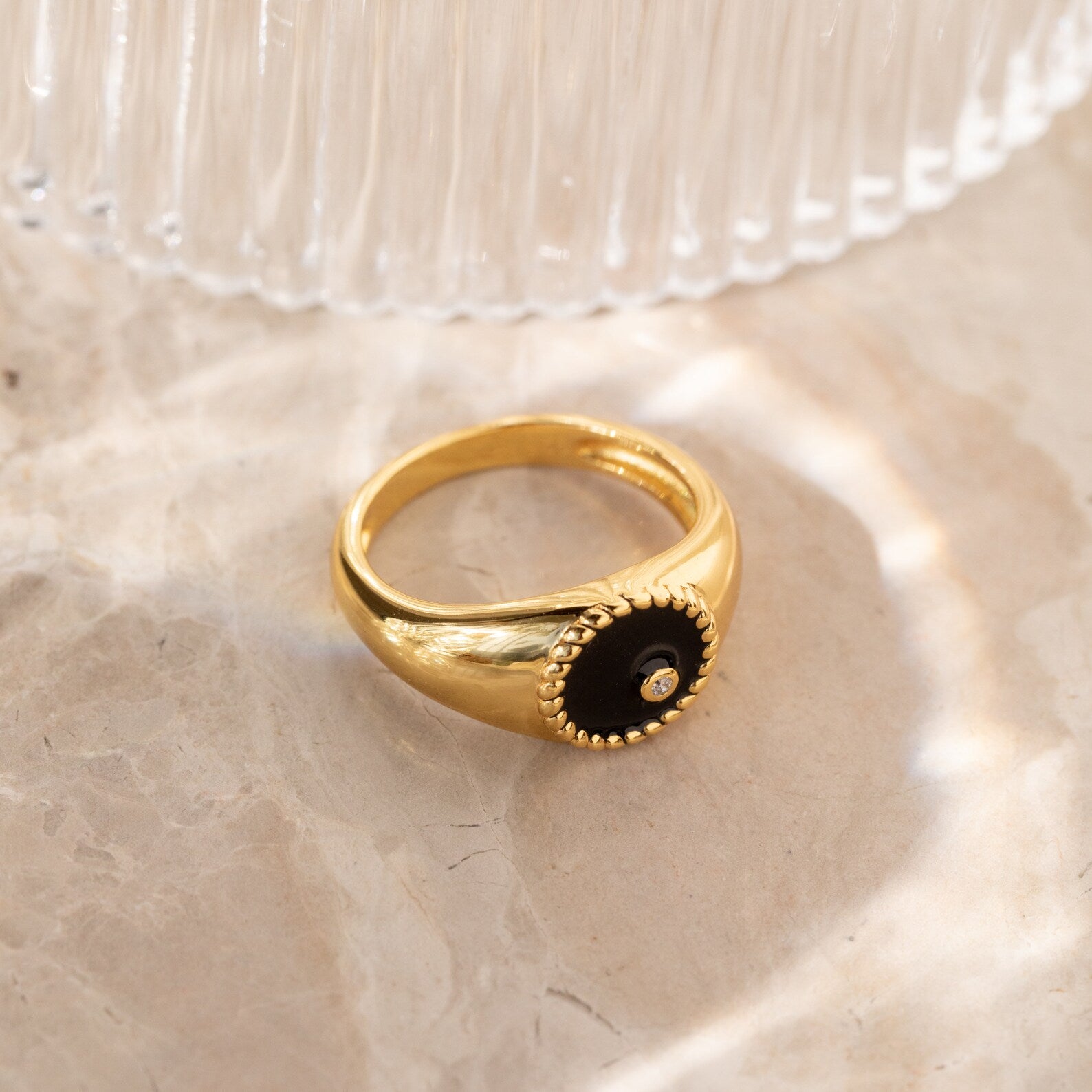 The Natasha Black Signet Ring features a black circular center with a small CZ diamond, elegantly displayed on marble.