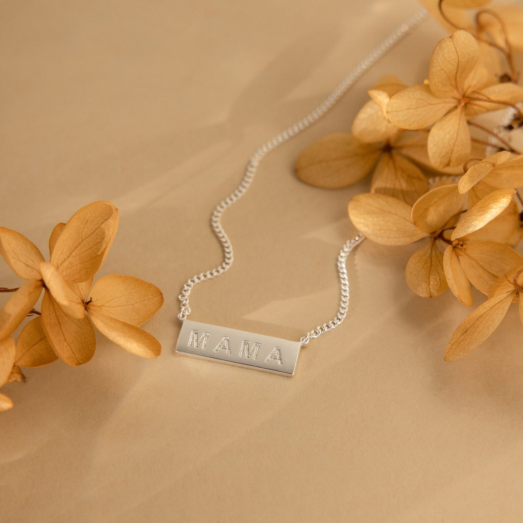 Dainty Bar Name Necklace in silver displayed on a beige surface with dried tan flowers, offering a personalized touch that's perfect for gifting.