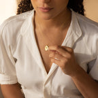 A woman in a white shirt holds the Eliza Oval Locket Necklace near her chest, highlighting its sentimental charm.