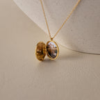 The Crystal Locket Necklace opens to reveal a small photo inside, displayed on a lightly textured surface.