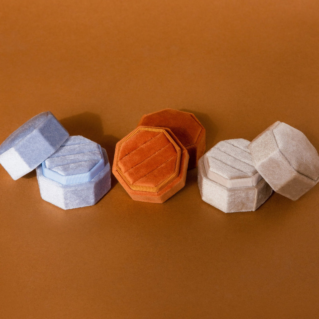 The 3 Slot Velvet Ring Box, shown in light blue, orange, and beige hexagonal designs on a brown surface, offers a stylish way to organize and display your favorite rings.