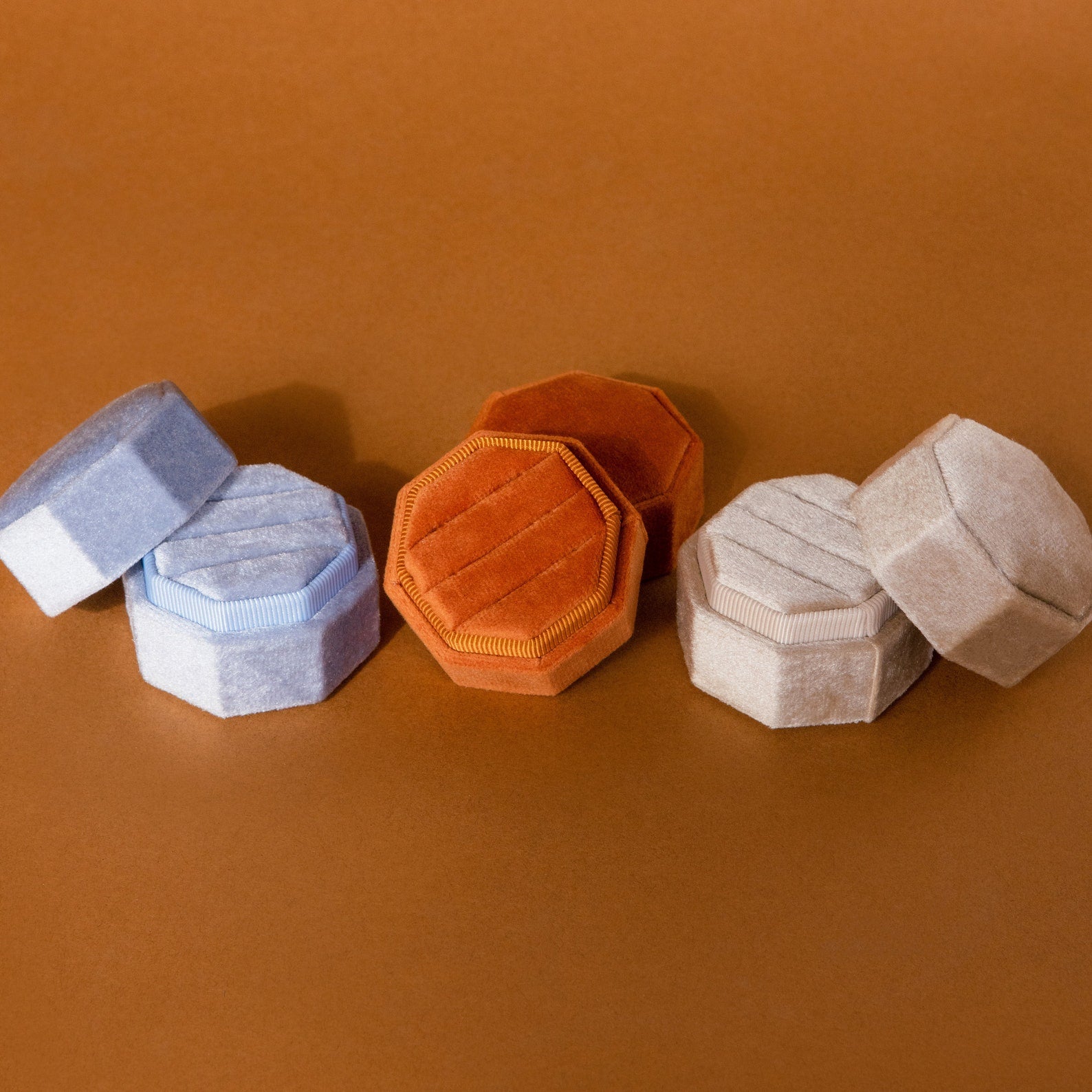 The 3 Slot Velvet Ring Box, shown in light blue, orange, and beige hexagonal designs on a brown surface, offers a stylish way to organize and display your favorite rings.