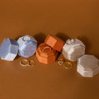 Mystery Ring Box: Assorted gold and diamond rings are displayed in luxurious velvet hexagonal boxes on a brown surface, each ring nestled in its own elegant Mystery Ring Box.