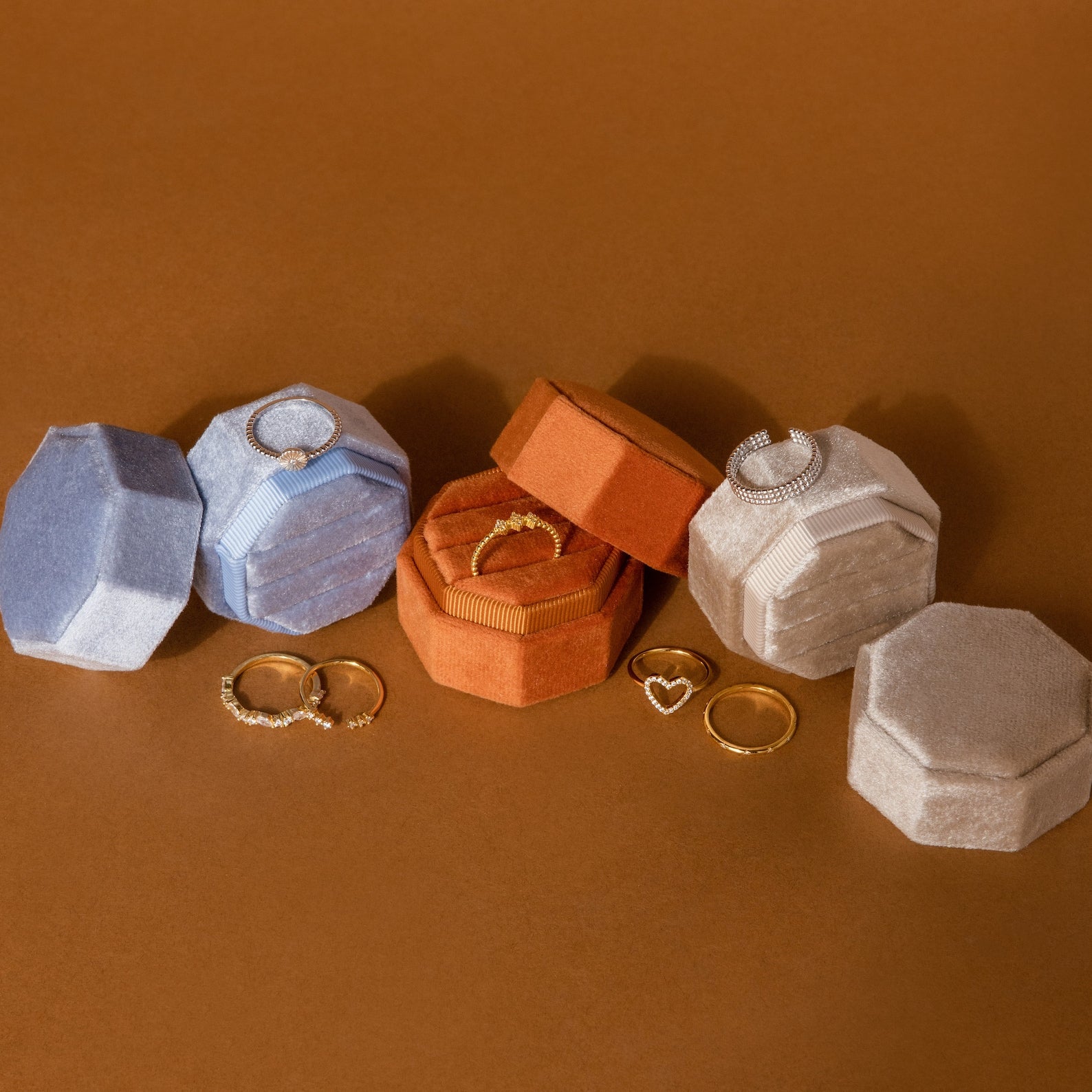 Mystery Ring Box: Assorted gold and diamond rings are displayed in luxurious velvet hexagonal boxes on a brown surface, each ring nestled in its own elegant Mystery Ring Box.