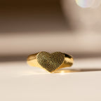 The Fingerprint Heart Signet Ring features a delicately engraved heart-shaped top with your unique fingerprint—a meaningful, personalized gift for mom. Displayed on a light surface, it’s the perfect keepsake.