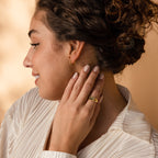 Woman with curly hair in a white blouse touches her ear, showcasing gold earrings and the Fingerprint Heart Signet Ring—a unique and elegant piece that's a thoughtful gift for mom.
