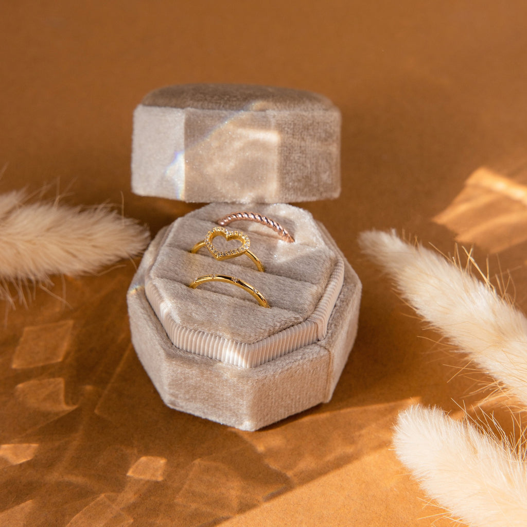 The Mystery Ring Box features three gold rings in a velvet case, showcased in a hexagonal box with beige decor and warm lighting.