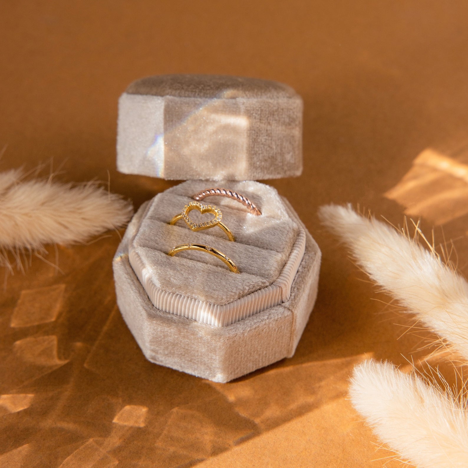 The Mystery Ring Box features three gold rings in a velvet case, showcased in a hexagonal box with beige decor and warm lighting.