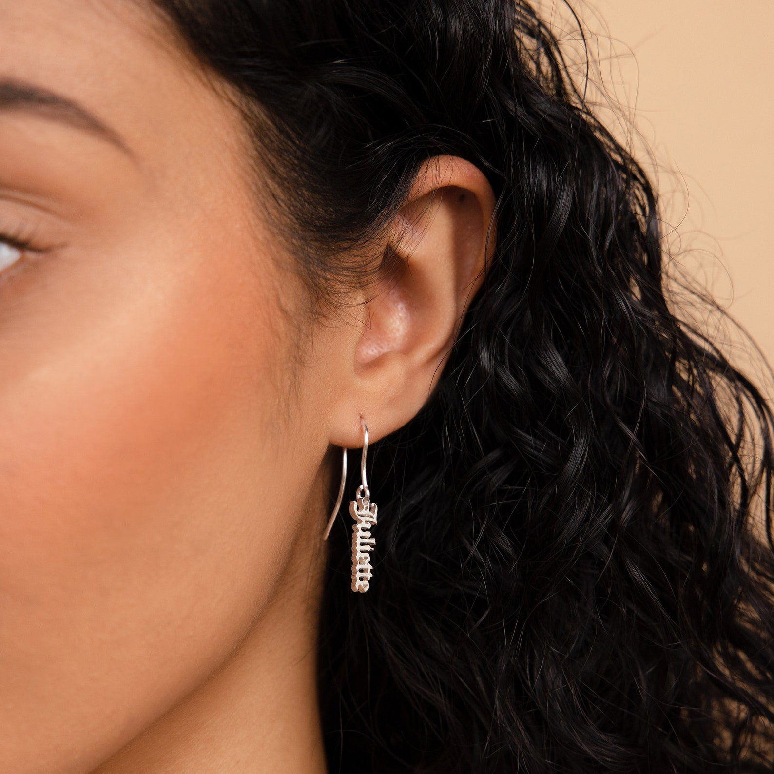 A close up of a woman's ear adorned with Old English Dangling Name Earrings.