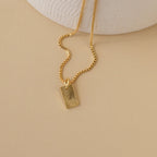 The Mini Fingerprint Tag Necklace features a rectangular, engraved pendant for a personalized touch—elegantly displayed on a beige surface. A thoughtful Mother's Day gift.
