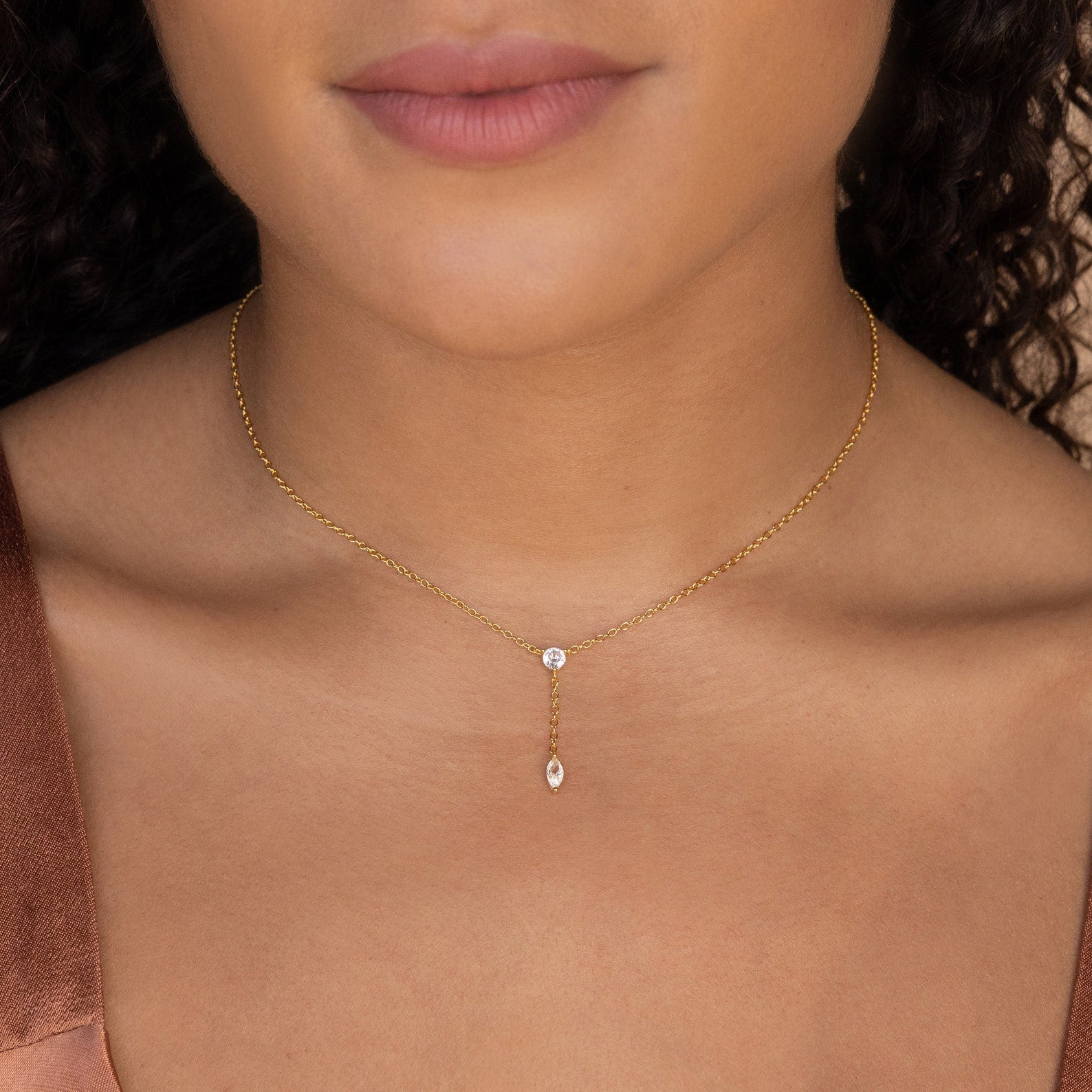 A woman shown from the shoulders up wears the Leena Diamond Lariat Necklace, featuring a gold delicate chain and two small dangling diamond stones.