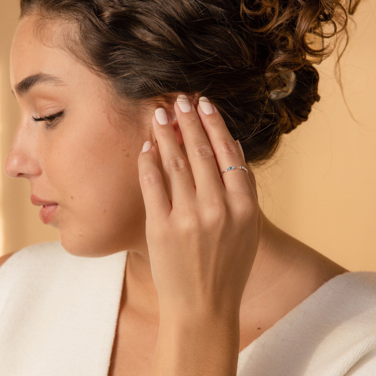 A woman with curly hair touches her ear, highlighting the Duo Marquise Birthstone Ring—a slim, personalized silver band—on her finger.