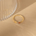 The Duo Marquise Birthstone Ring, featuring two small gemstones, rests on a beige surface beside a ribbed glass object.