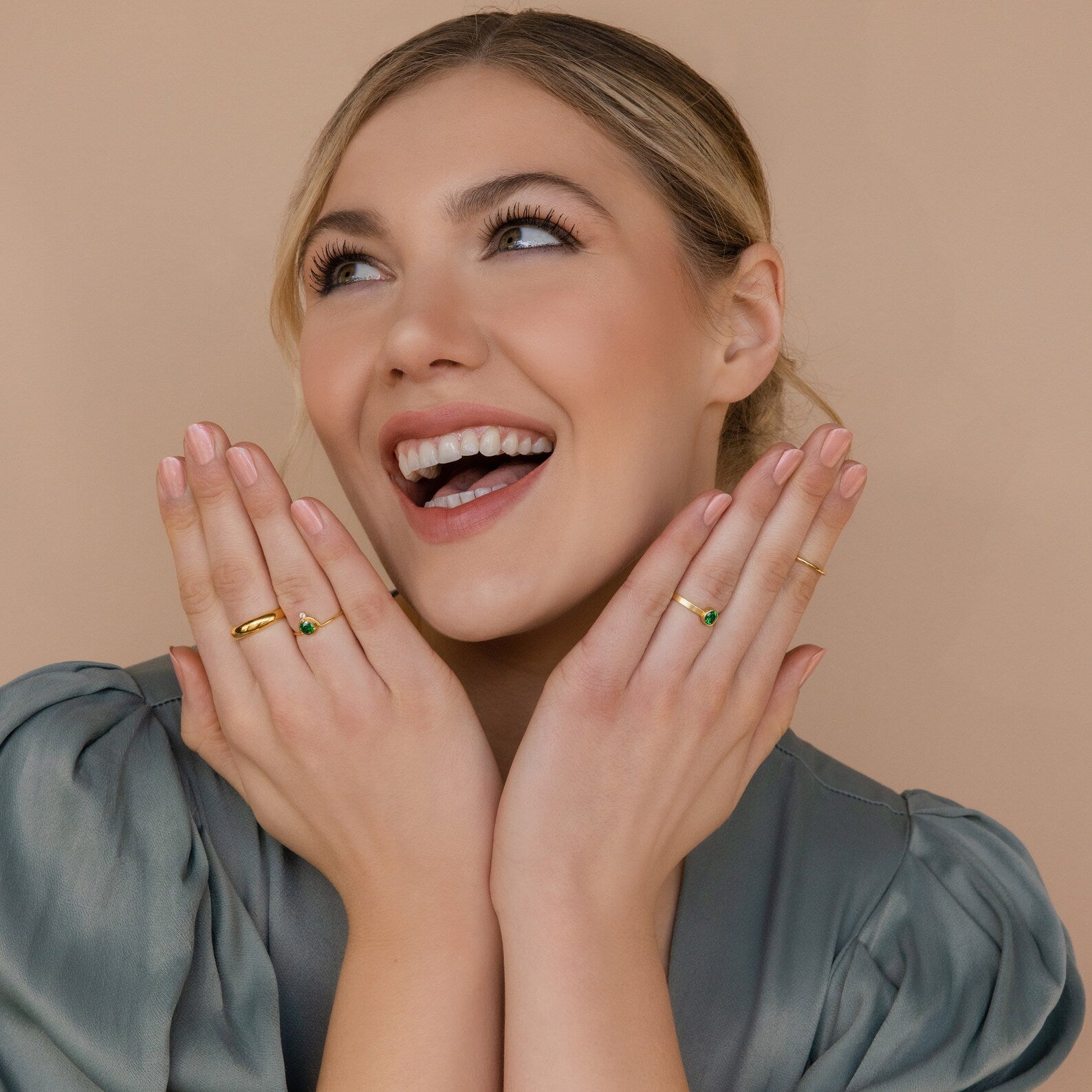 Smiling woman in a green satin blouse, wearing the Duo Vintage Birthstone Ring—ideal as a new mom gift or Mother’s Day present—posing on a beige background with her hands near her face.