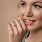 A woman smiles, touching her face and wearing the Duo Vintage Birthstone Ring with a green gemstone—a stylish personalized gift for Mother's Day.