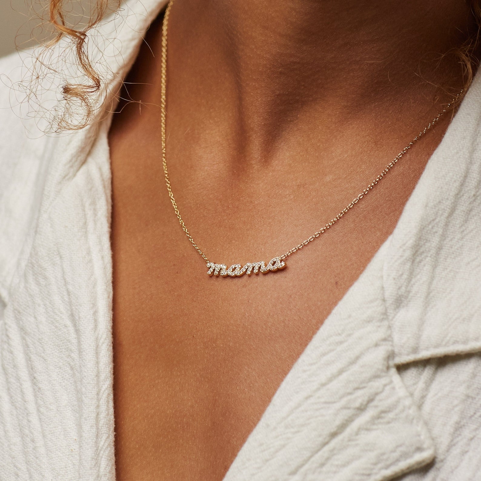 A person wears a gold cursive Mama Necklace, crafted from 925 Sterling Silver, paired with a cream-textured shirt—an ideal gift for mom.
