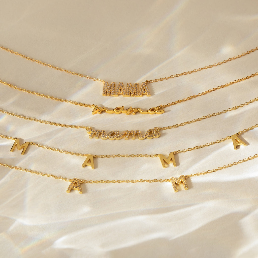 Five gold Mama Necklaces in different fonts and styles lie on a satin-like surface—an ideal gift for Mom that brings a heartfelt touch to her jewelry collection.