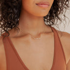 A woman in a rust-colored tank top wearing a gold Mama Necklace—Mama Necklaces make the perfect gift for Mom.