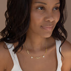 A woman wears the Grace Name Heart Necklace personalized with "Mama" and two other names, paired with a white tank top.
