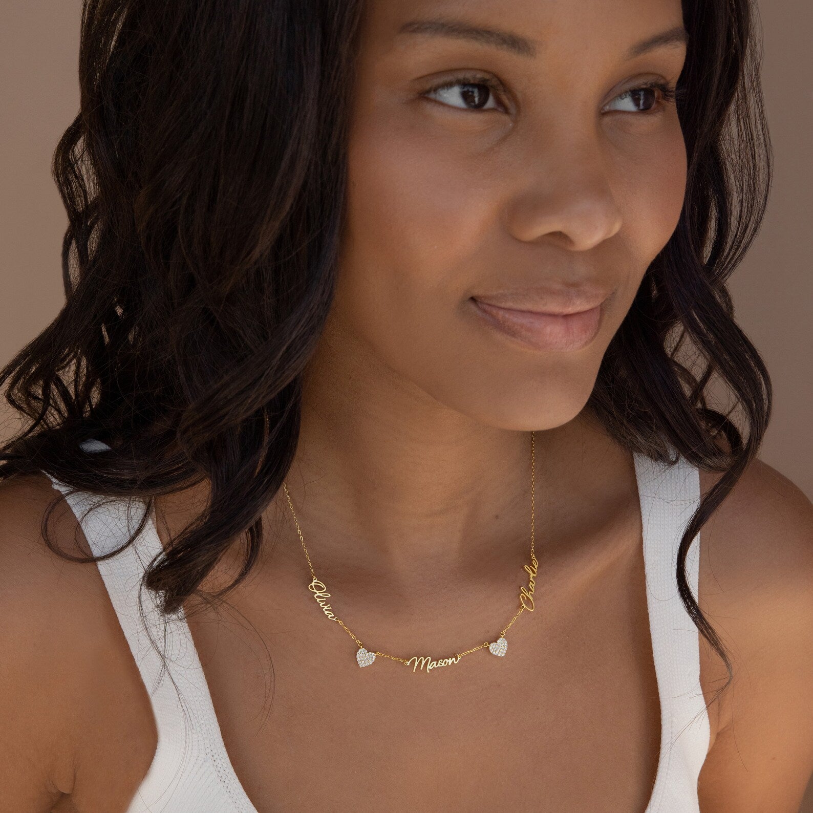 A woman wears the Grace Name Heart Necklace personalized with "Mama" and two other names, paired with a white tank top.