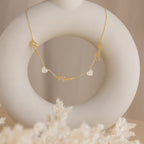 The Grace Name Heart Necklace features three personalized names—Olivia, Mason, and Charlie—with two heart charms, elegantly displayed on a white sculpture.