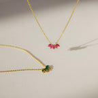 Two delicate gold chain necklaces, one featuring a pink gemstone and the other the Marquise Birthstone Necklace with a green stone, displayed on a light surface.