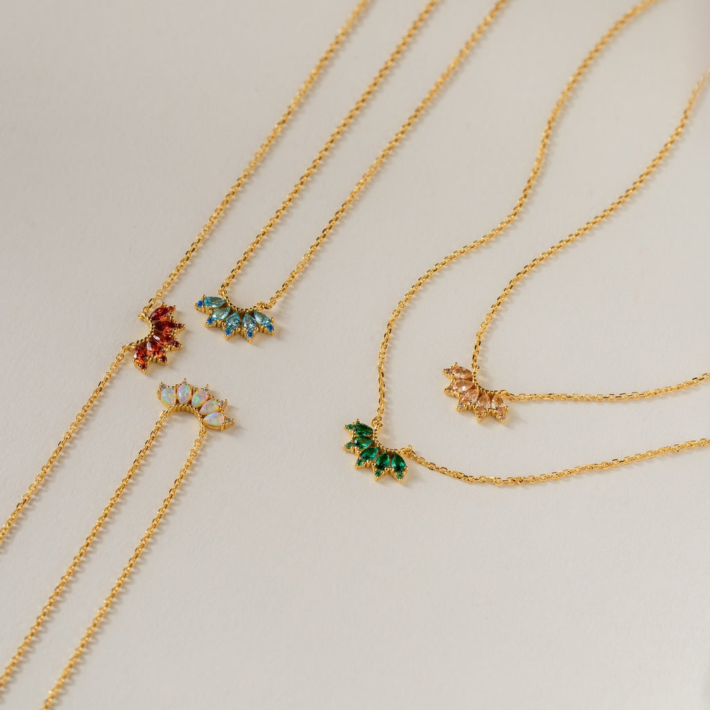 The Marquise Birthstone Necklace, adorned with a colorful pendant, is elegantly arranged on a light beige surface.