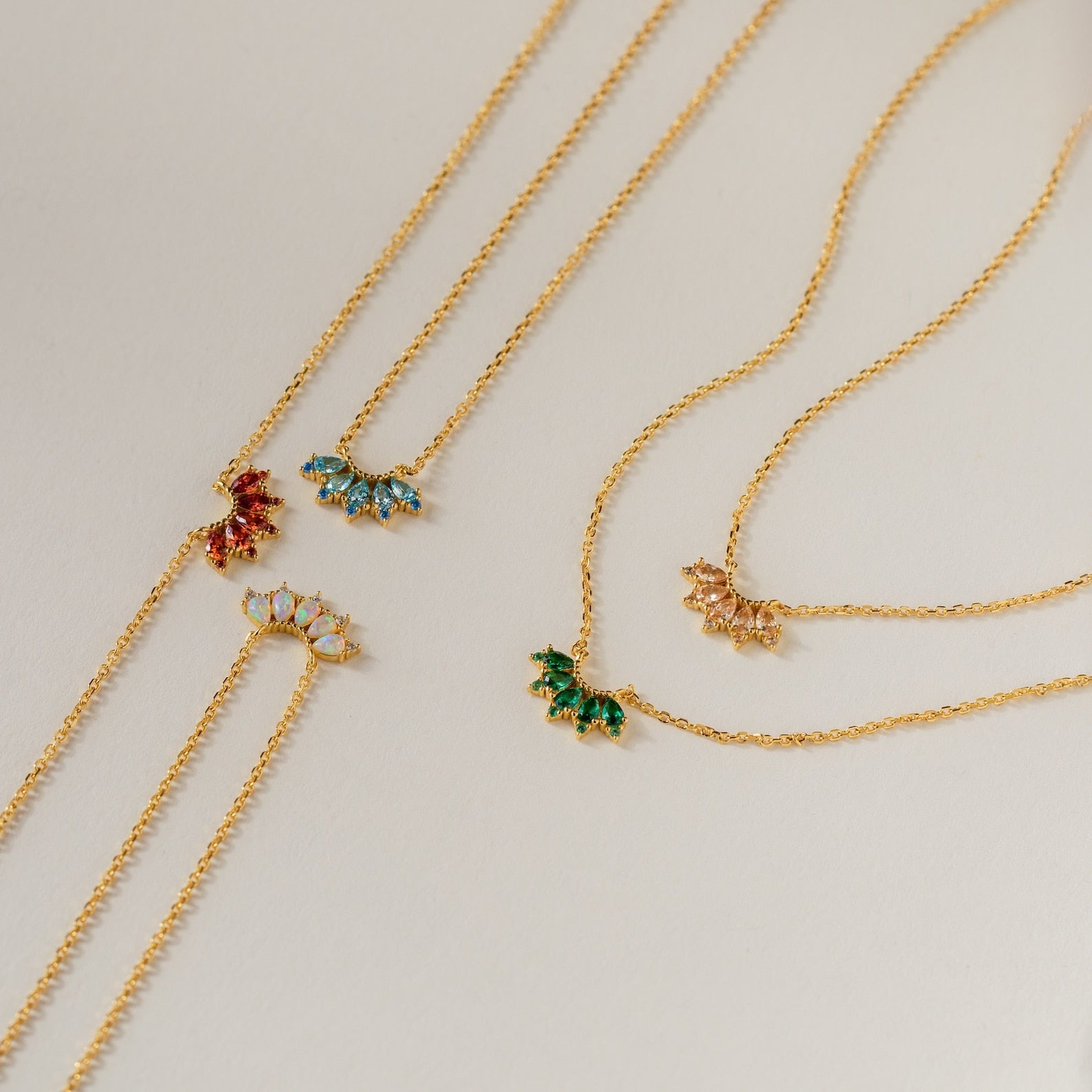 The Marquise Birthstone Necklace, adorned with a colorful pendant, is elegantly arranged on a light beige surface.