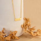 Dainty Bar Name Necklace featuring a rectangular 11:11 pendant in gold, displayed on a white vase with dried beige flowers.