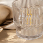 Two pairs of Minimal Dangling Name Earrings—one silver, one gold—are displayed on a ribbed glass cup with a beige satin backdrop, making them the perfect unique bridesmaid gift.