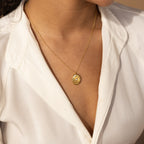 A woman in a white blouse wears the elegant Eliza Oval Locket Necklace on her chest, adding a touch of timeless charm.