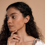 A woman with curly hair wears Grace Name Earrings and a gold ear cuff, gazing to the side with her hand near her chin.
