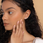 A woman with curly hair touches her face, elegantly showing off Mellow Name Earrings—a personalized custom gift that shines with individuality.