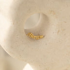 Old English Name Earrings displayed in a circular indentation on a textured, light stone surface—a stunning custom gift that pairs beautifully with personalized rings or name stud earrings.