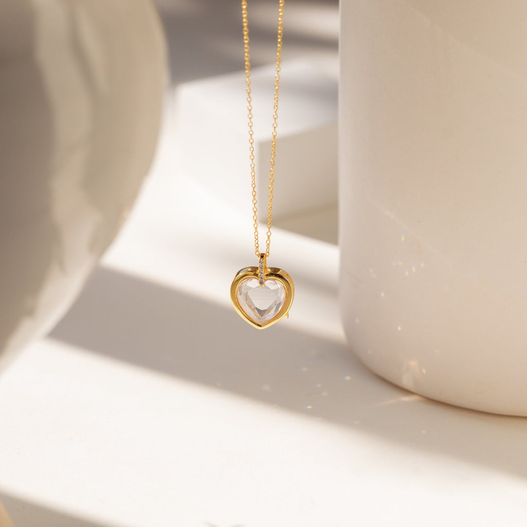 Crystal Locket Necklaces feature a gold chain and heart-shaped pendant, beautifully showcased in soft, natural light against a neutral background.